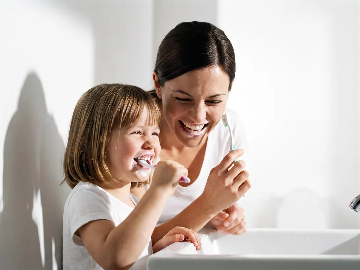 Una mamá y su hija riendo mientras se cepillan los dientes