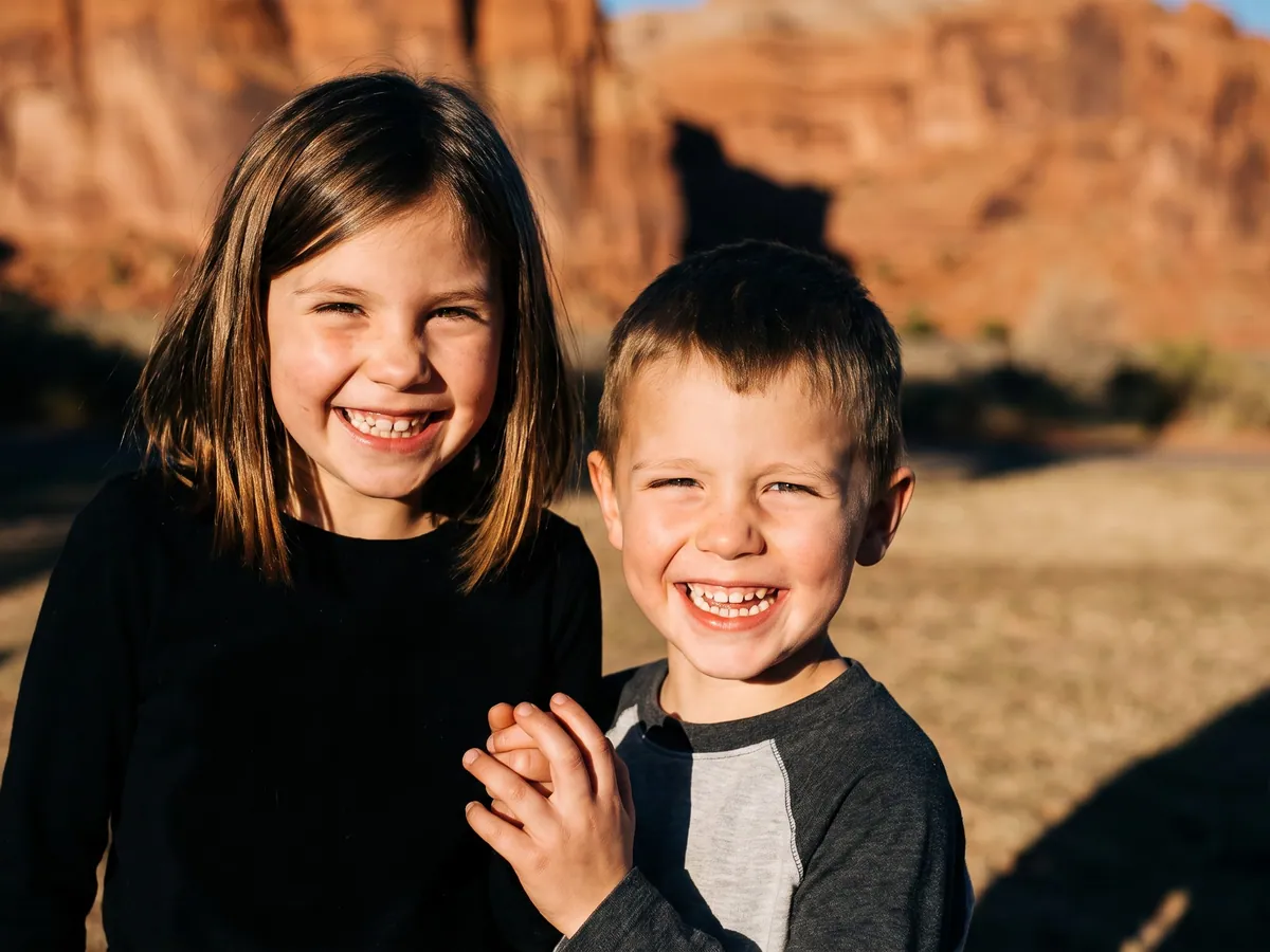 Dos niños sonriendo en un parque bajo los acantilados de roca roja